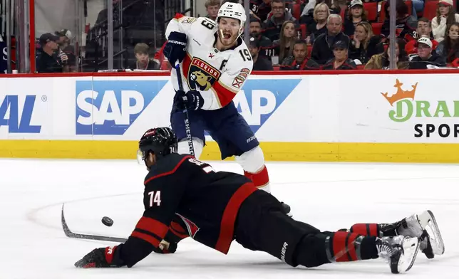 Florida Panthers' Matthew Tkachuk (19) passes the puck around a sliding Carolina Hurricanes' Jaccob Slavin (74) during the third period of Game 2 of the NHL hockey Stanley Cup Eastern Conference finals in Raleigh, N.C., Thursday, May 22, 2025. (AP Photo/Karl DeBlaker)