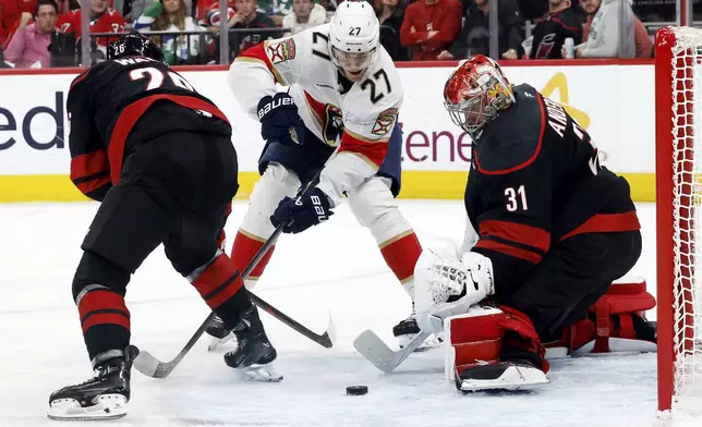 Florida Panthers' Eetu Luostarinen (27) looses control of the puck skating between Carolina Hurricanes' Sean Walker (26) and goaltender Frederik Andersen (31) during the first period of Game 2 of the NHL hockey Stanley Cup Eastern Conference finals in Raleigh, N.C., Thursday, May 22, 2025. (AP Photo/Karl DeBlaker)