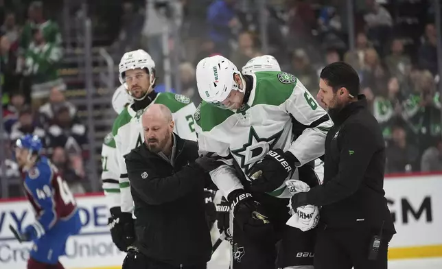 Dallas Stars defenseman Lian Bichsel, center, is helped off the ice by trainers after being injured in the second period of Game 6 of an NHL hockey first-round playoff series against the Colorado Avalanche, Thursday, May 1, 2025, in Denver. (AP Photo/David Zalubowski)