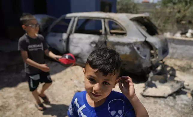 Palestinian boys play by their family's vehicle, which was burnt during an overnight attack by Israeli settlers and left several burnt vehicles and damaged homes, residents said, in the West Bank village of Bruqin, near Salfit, Friday, May 23, 2025. (AP Photo/Nasser Nasser)