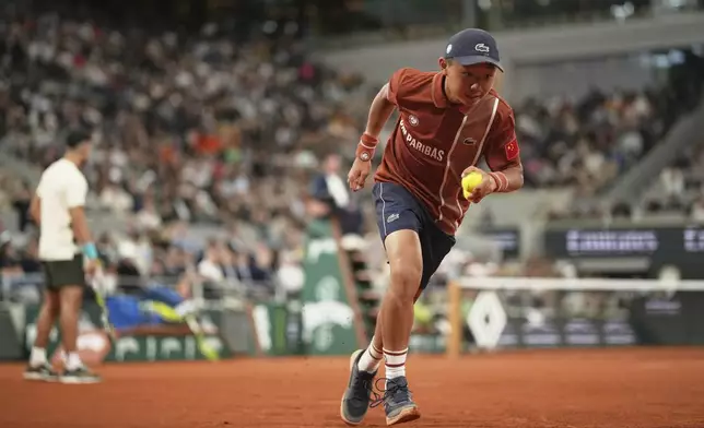 A ball boy runs while Spain's Carlos Alcaraz, background left, plays Hungary's Fabian Maroszan during their second round match of the French Tennis Open, at the Roland-Garros stadium, in Paris, Wednesday, May 28, 2025. (AP Photo/Christophe Ena)