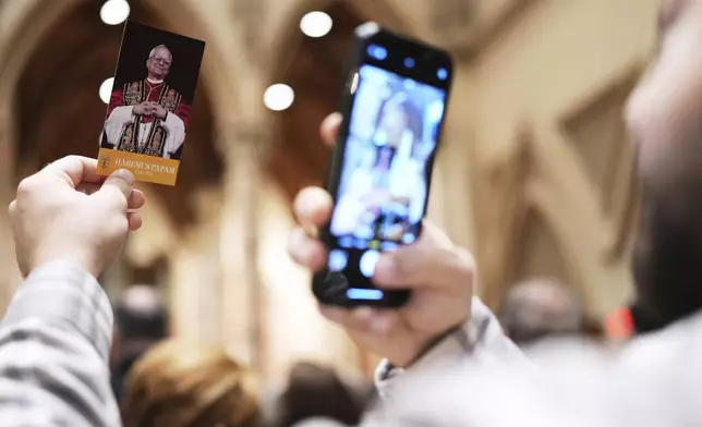 A man takes a picture of a brochure that reads "A prayer of thankfulness for the election of Pope Leo XIV" during a mass at Holy Name Cathedral in Chicago, Sunday, May 11, 2025. (AP Photo/Nam Y. Huh)