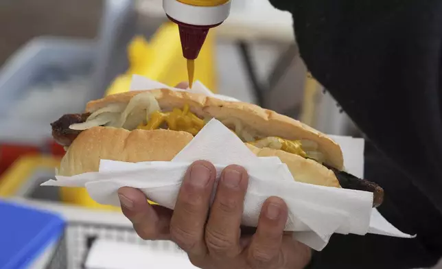 A customer pours mustard over a sausage in a bread roll outside a polling booth at Sydney's Bondi Beach, Saturday, May 3, 2025. (AP Photo/Mark Baker)