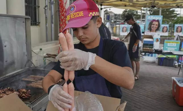 A volunteer prepares to cook sausages on a BBQ outside a polling booth at Sydney's Bondi Beach, Saturday, May 3, 2025. (AP Photo/Mark Baker)