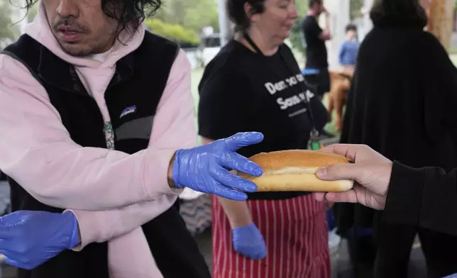 A worker hands a man a "Democracy Sausage" at the Marrickville Public School in Sydney, Australia, Saturday, May 3, 2025, after voting in the general election. (AP Photo/Rick Rycroft)