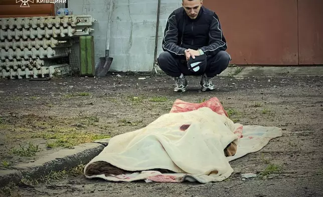 In this photo provided by the Ukrainian Emergency Service, a man reacts at the body of a killed resident following Russia's drone attack in the Kyiv region, Ukraine, Sunday, May 18, 2025. (Ukrainian Emergency Service via AP)