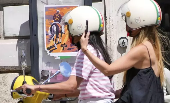 Tourists ride a Vespa scooter past a poster showing Pope Leo XIV wearing a jersey with the No War sign and riding a horse on the Franciscus' path on the eve of Pontiff installation mass, in Rome, Saturday, May 17, 2025. (AP Photo/Gregorio Borgia)