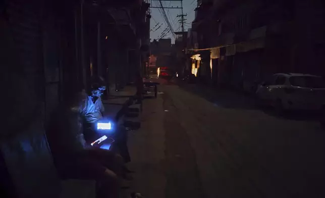 People browse their mobile phones for news updates sitting outside closed shops during a black out in Jodhpur, in the Indian state of Rajasthan, Thursday, May 8, 2025. ( AP Photo/Himanshu Vyas )