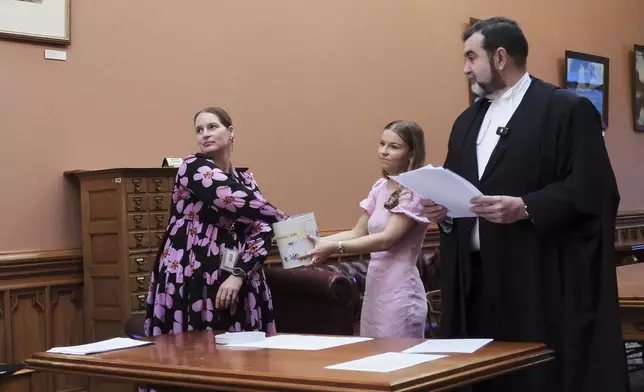 Parliamentary Service staffer Renee Beeson, left, draws a bingo token from the biscuit tin, observed by Chloe French and Clerk of the New Zealand House of Representatives David Wilson at Parliament in Wellington, New Zealand, Thursday, May 22, 2025. (AP Photo/Charlotte Graham-McLay)