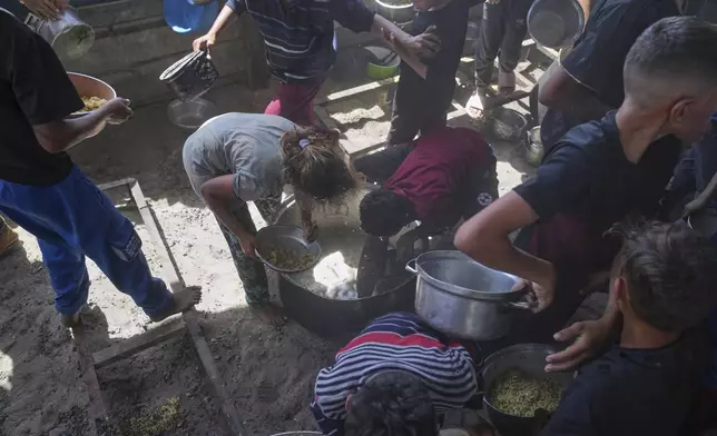 Palestinian children scrape a pot for leftover food after all meals were distributed at a community kitchen in Khan Younis, southern Gaza Strip, on Friday, May 9, 2025. (AP Photo/Abdel Kareem Hana)