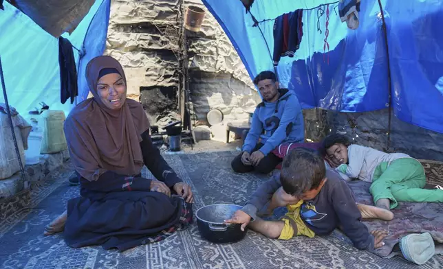 Ward Nar, left, reacts as she speaks with the photographer after returning empty-handed from attempting to receive donated food for her family, including her husband Mohammed Zaharna (center right) and their children, Sally (right) and Raed, at a community kitchen in Khan Younis, in the southern Gaza Strip, Friday, May 9, 2025. (AP Photo/Abdel Kareem Hana)