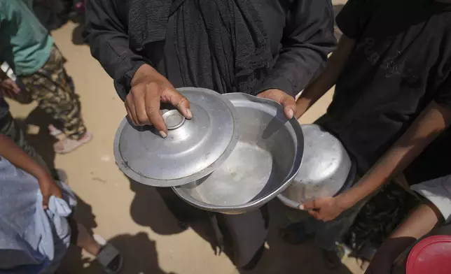 A woman shows up her empty pot after a community kitchen ran out of donated food to distribute in Khan Younis, in the southern Gaza Strip, Friday, May 9, 2025. (AP Photo/Abdel Kareem Hana)