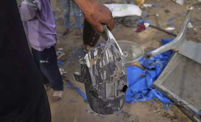 A man holds a piece of an explosive device as Palestinians inspect the damage caused by an Israeli strike that hit tents near Al-Aqsa Hospital in Deir al-Balah, in the central Gaza Strip, Saturday, May 17, 2025. (AP Photo/Abdel Kareem Hana)