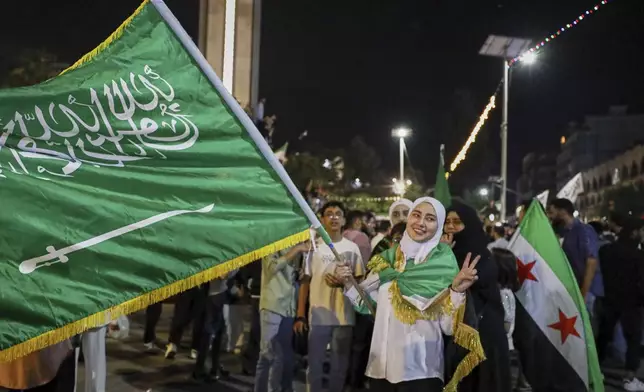 A girl holds a Saudi flag in celebration after U.S. President Donald Trump announced plans during his visit to Saudi Arabia to ease sanctions on Syria and normalize relations with its new government, in Homs, Syria, late Tuesday, May 13, 2025.(AP Photo/Omar Albam)