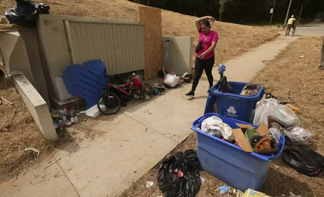 A pedestrian walks past trash left outside a bin near a homeless encampment, Monday, May 12, 2025, in Los Angeles. (AP Photo/Damian Dovarganes)