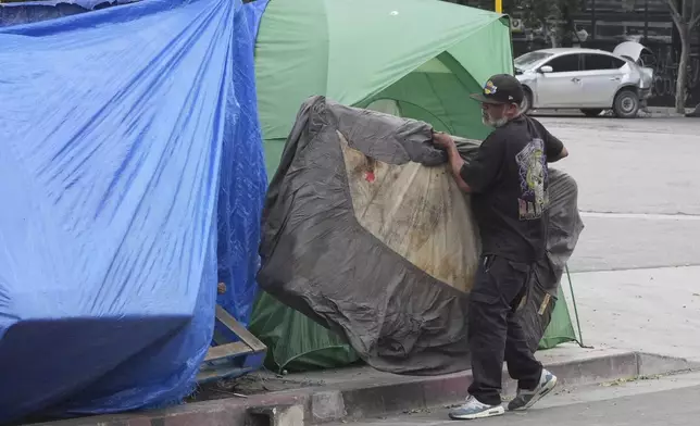 A man carries a mattress into a tent set up on a sidewalk, Monday, May 12, 2025, in Los Angeles. (AP Photo/Damian Dovarganes)