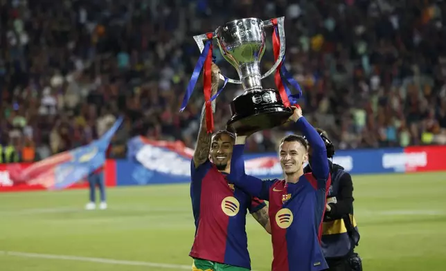 Barcelona's Raphinha, left, and Marc Casado celebrate with the trophy after the La Liga after the Spanish La Liga soccer match between Barcelona and Villarreal at Lluis Companys Olympic Stadium in Barcelona, Spain, Sunday, May 18, 2025. (AP Photo/Joan Monfort)