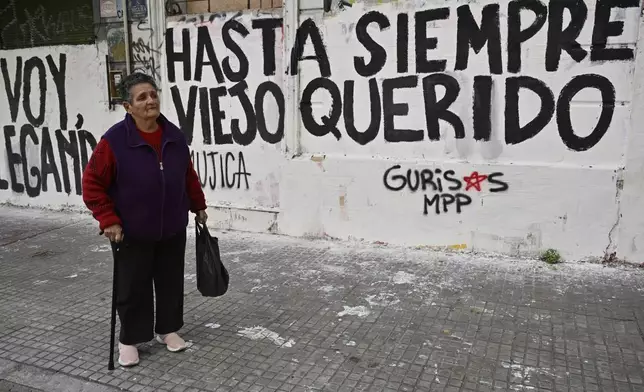 A woman watches the funeral procession of former President Jose Mujica from the presidential palace to the National Assembly, next to graffiti that reads in Spanish: "Farewell dear old man," in Montevideo, Uruguay, Wednesday, May 14, 2025. (AP Photo/Santiago Mazzarovich)