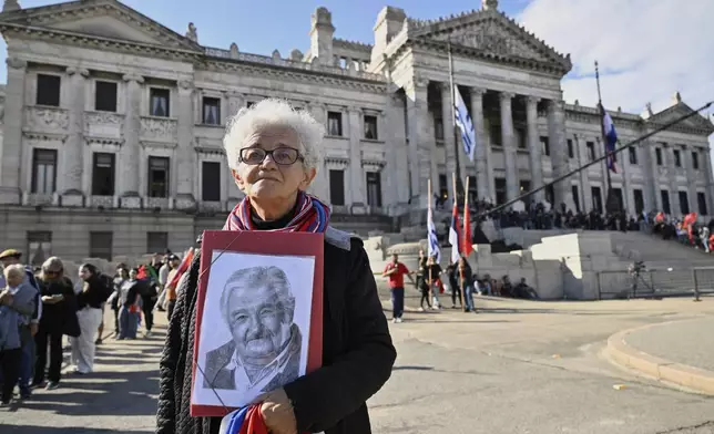 A woman holds a portrait of Uruguay's former President Jose Mujica outside the Legislative Palace, where he lies in state during funeral ceremonies in Montevideo, Uruguay, Wednesday, May 14, 2025. (AP Photo/Santiago Mazzarovich)