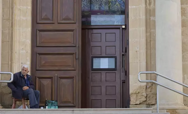 A man sits outside St. George Church in the Maronite village of Kormakitis in the breakaway north of the ethnically divided Cyprus on Wednesday, April 23, 2025. (AP Photo/Petros Karadjias)