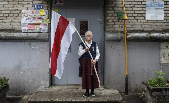 FILE - Nina Bahinskaya, 73, poses for a photo holding a flag that became the symbole of the opposition at an entrance of her apartment building in Minsk, Belarus, on Sept. 10, 2020. (AP Photo, File)