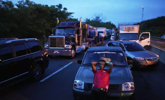 A driver leans on his vehicle as traffic backs up on the Pan-American Highway, blocked by anti-government protesters opposing social security reforms and a Panama-U.S. memorandum concerning the Panama Canal, in El Piro, Panama, Wednesday, May 14, 2025. (AP Photo/Matias Delacroix)