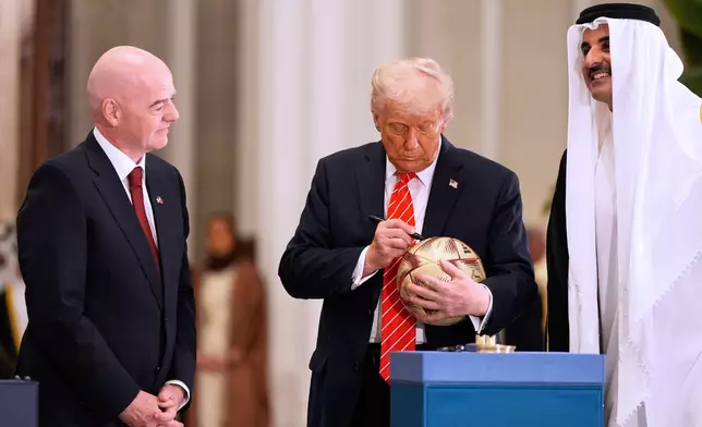 President Donald Trump signs a FIFA soccer ball as Qatar's Emir Sheikh Tamim bin Hamad Al Thani and FIFA President Gianni Infantino looks on at the Lusail Palace, Wednesday, May 14, 2025, in Doha, Qatar, as they marked the passing of World Cup hosting duties from Qatar, which held it in 2022, to the United States, which is hosting in 2026. (AP Photo/Alex Brandon)