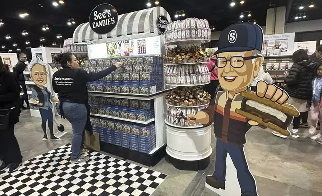 A See's Candy worker restocks the display next to a cutout of Warren Buffett at the Berkshire Hathaway shareholders meeting exhibit hall Friday, May 2, 2025 in Omaha, Neb. (AP Photo/Josh Funk)