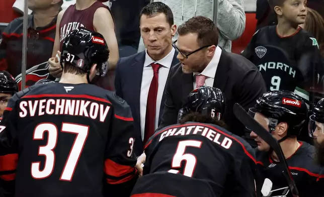 Carolina Hurricanes head coach Rod Brind'Amour, left, and assistant couch Tim Gleason, right, speak to the team during a timeout in the third period of Game 2 of an NHL hockey Stanley Cup first-round playoff series against the New Jersey Devils in Raleigh, N.C., Tuesday, April 22, 2025. (AP Photo/Karl DeBlaker)
