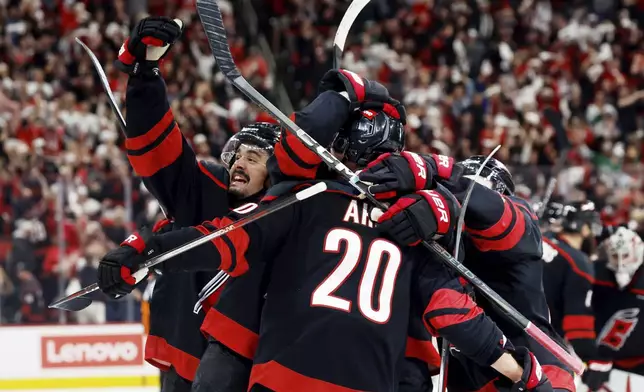 Carolina Hurricanes' Seth Jarvis, left, salutes the crowd from the celebration of Sebastian Aho's game-winning goal during the second overtime period of Game 5 of an NHL hockey Stanley Cup first-round playoff series against the New Jersey Devils in Raleigh, N.C., Tuesday, April 29, 2025. (AP Photo/Karl DeBlaker)