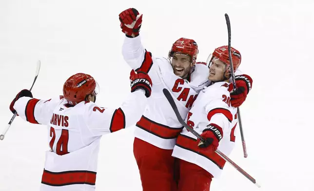 Carolina Hurricanes center Sebastian Aho, right, celebrates with Shayne Gostisbehere (4) and Seth Jarvis (24) after scoring against the New Jersey Devils during the third period of Game 3 of a first-round NHL hockey playoff series Friday, April 25, 2025, in Newark, N.J. (AP Photo/Noah K. Murray)