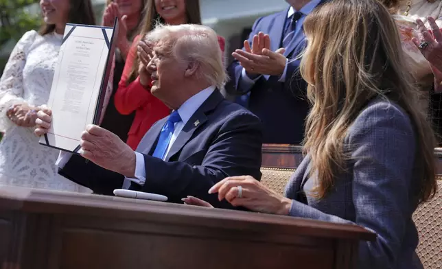 President Donald Trump holds up a bill for the "Take it Down Act" that he and first lady Melania Trump, right, signed in the Rose Garden of the White House, Monday, May 19, 2025, in Washington. (AP Photo/Evan Vucci)