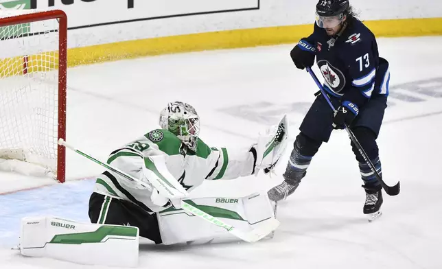 Dallas Stars goaltender Jake Oettinger (29) makes a save on a Winnipeg Jets shot as Brandon Tanev (73) looks for the rebound during third period NHL playoff hockey action in Winnipeg, Thursday, May 15, 2025. (Fred Greenslade/The Canadian Press via AP)