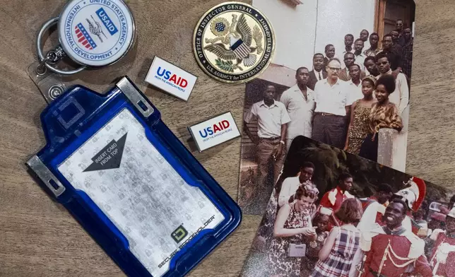 Anna Eisenberg's empty USAID badge holder is seen next to USAID pins, a coin from the USAID Office of Inspector General awarded to her mother, Cathy Votaw, and photographs of her grandfather, Albert Votaw, and his family during his service with USAID in West Africa circa 1968, Thursday, Feb. 27, 2025, in Washington. (AP Photo/Jacquelyn Martin)
