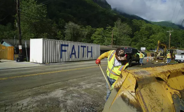 David Cruz mixes cement in the bucket of an end loader for a sewer manhole on Main Street in Chimney Rock Village, N.C., on Wednesday, May 14, 2025. (AP Photo/Allen G. Breed)