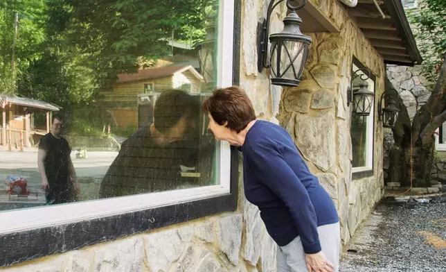 Novelist Rose Senehi peeks into the window of a flood-damaged shop on Main Street in Chimney Rock Village, N.C., on Tuesday, May 13, 2025. (AP Photo/Allen G. Breed)