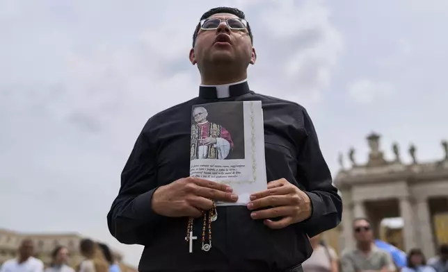 A priest holds a rosary and a newspaper showing a picture of Pope Leo XIV as he appears at the central balcony of St. Peter's Basilica for his first Sunday blessing after his election, in St. Peter's Square at the Vatican, Sunday, May 11, 2025.(AP Photo/Bernat Armangue)