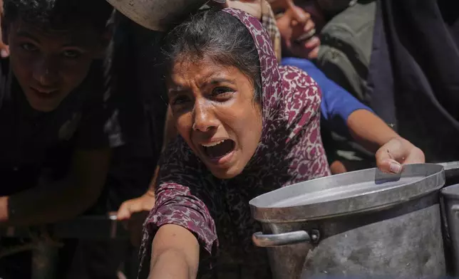Palestinians struggle to receive cooked food distributed at a community kitchen in the Muwasi area of Khan Younis, in the Gaza Strip, Friday, May 23, 2025. (AP Photo/Abdel Kareem Hana)