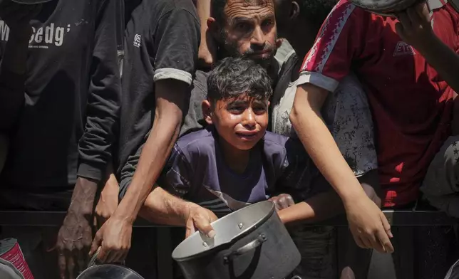 Palestinians struggle to receive cooked food distributed at a community kitchen in the Muwasi area of Khan Younis, in the Gaza Strip, Friday, May 23, 2025. (AP Photo/Abdel Kareem Hana)