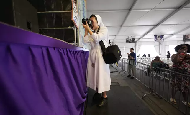 Sister Boram Lee, a Catholic nun with the Salesian Sisters, stands on a pedestal while photographing the Academy Of Our Lady High School gospel choir at the New Orleans Jazz &amp; Heritage Festival in New Orleans, Friday, April 25, 2025. (AP Photo/Gerald Herbert)