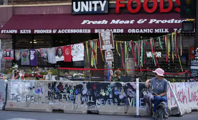 A woman with a dog visits the spot of George Floyd's murder at George Floyd Square on the five-year anniversary of Floyd's death, Sunday, May 25, 2025, in Minneapolis. (AP Photo/Abbie Parr)