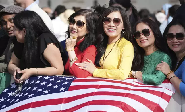 Faithful stand by a United States flag ahead of Pope Leo XIV's formal inauguration of his pontificate with a Mass in St. Peter's Square, at the Vatican, Sunday, May 18, 2025. (AP Photo/Andrew Medichini)