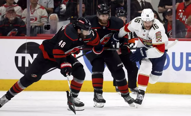Florida Panthers' Aleksander Barkov (16) chases the puck with Carolina Hurricanes' Jordan Staal, center, and Jordan Martinook (48) nearby during the first period of Game 2 of the NHL hockey Stanley Cup Eastern Conference finals in Raleigh, N.C., Thursday, May 22, 2025. (AP Photo/Karl DeBlaker)