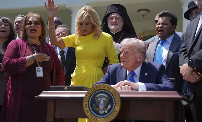 President Donald Trump sits at a desk as he and religious leaders listen to a musical performance before Trump signs an executive order during a National Day of Prayer event in the Rose Garden of the White House, Thursday, May 1, 2025, in Washington. (AP Photo/Evan Vucci)