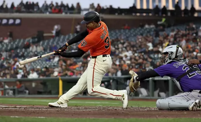 San Francisco Giants' LaMonte Wade Jr., left, hits an RBI double in front of Colorado Rockies catcher Jacob Stallings, right, during the second inning of a baseball game in San Francisco, Friday, May 2, 2025. (AP Photo/Jed Jacobsohn)