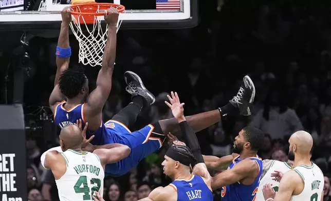New York Knicks forward OG Anunoby, top, hangs from the rim after dunking against the Boston Celtics during the second half of Game 1 of an NBA basketball second-round playoff series Monday, May 5, 2025, in Boston. (AP Photo/Charles Krupa)