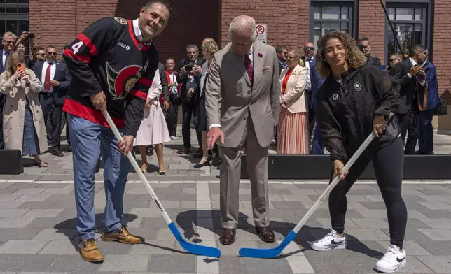 King Charles participate in a ceremonial puck drop with street hockey captains Chris Phillips, left and Desiree Scott during a visit to Lansdowne Park in Ottawa, Canada on Monday, May 26, 2025. (Christinne Muschi/The Canadian Press via AP)