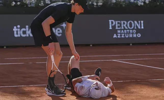 Italy's Jannik Sinner, standing, tends to Netherlands' Jesper De Jong who lies on the court after falling, during their tennis match at the Italian Open at the Foro Italico, in Rome, Monday, May 12, 2025. (AP Photo/Alessandra Tarantino)