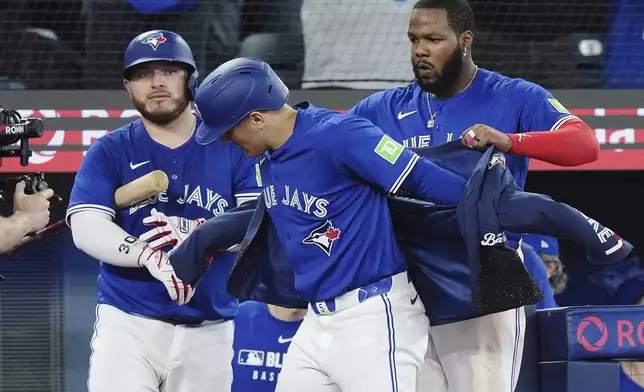 Toronto Blue Jays' Daulton Varsho, center, celebrates his grand slam against the San Diego Padres with Vladimir Guerrero Jr., right, and Alejandro Kirk during the eighth inning of a baseball game in Toronto on Wednesday, May 21, 2025. (Nathan Denette/The Canadian Press via AP)