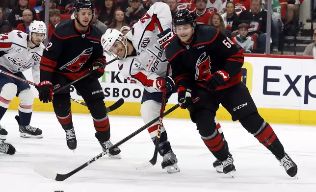 Carolina Hurricanes' Eric Robinson (50) battles for the puck with Washington Capitals' Nic Dowd (26) with Hurricanes' Jesperi Kotkaniemi (82) nearby during the first period of Game 4 of a second-round NHL hockey playoff series in Raleigh, N.C., Monday, May 12, 2025. (AP Photo/Karl DeBlaker)